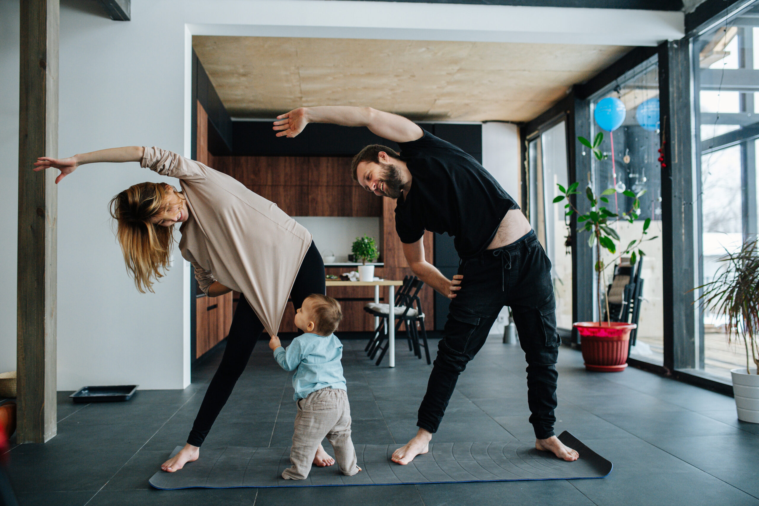 Parents doing yoga while baby pulls on mom's shirt