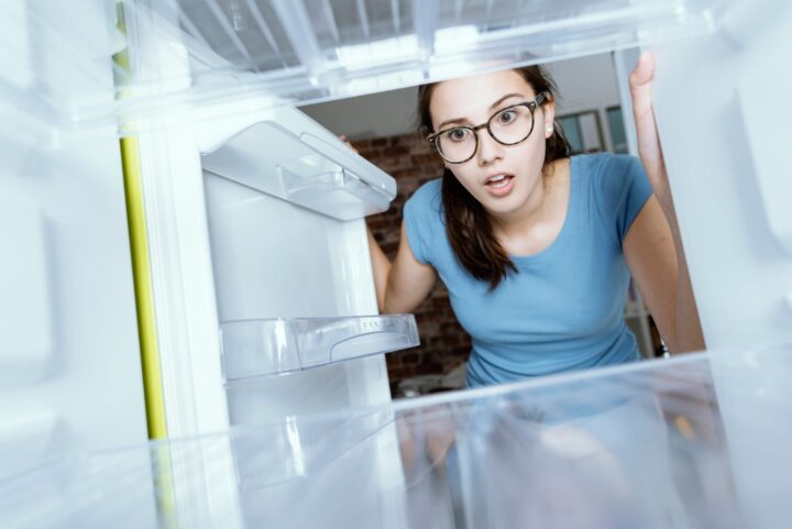 girl in blue shirt looking in empty fridge